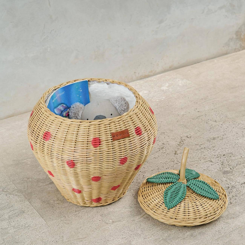 Opened Strawberry Rattan Storage Basket with a book, stuffed toy and a pouch inside, lid on the floor.