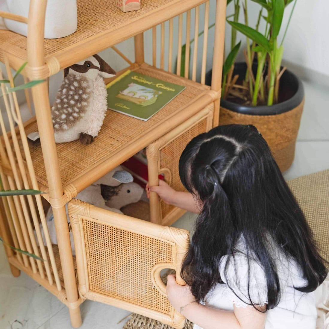 Close-up of a child opening one cabinet door of the Sunshine Arch Cabinet Shelf by MOMIJI, revealing toy storage inside.