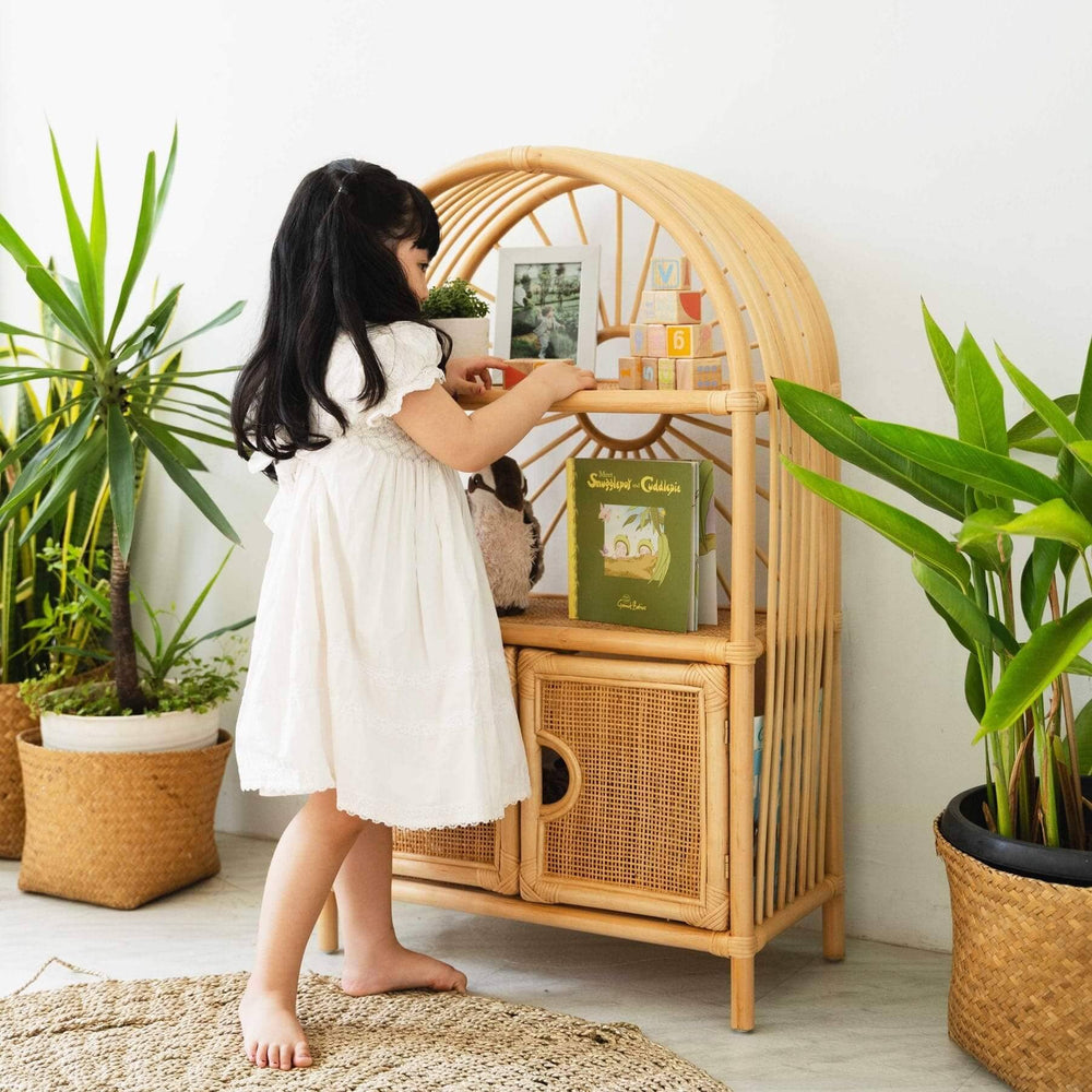 Child holding the upper shelf of the Sunshine Arch Cabinet Shelf by MOMIJI filled with colorful blocks, styled with rattan planters.