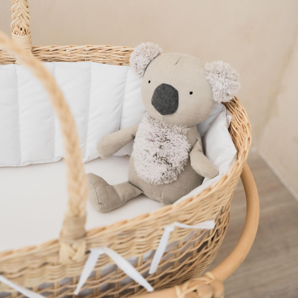 Koala doll placed inside the Vera Moses Rattan Basket by MOMIJI with white cushion, positioned on rattan stand.
