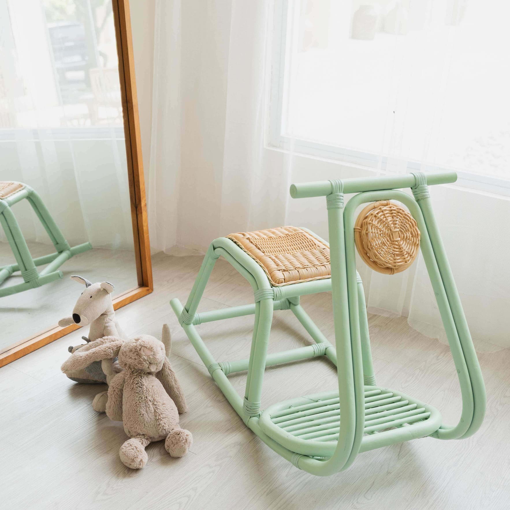 Vespa Rocker – Mint by MOMIJI placed on a light wooden floor in a room with a mirror and dolls, featuring a mint green frame with handwoven natural rattan seat and light detail.