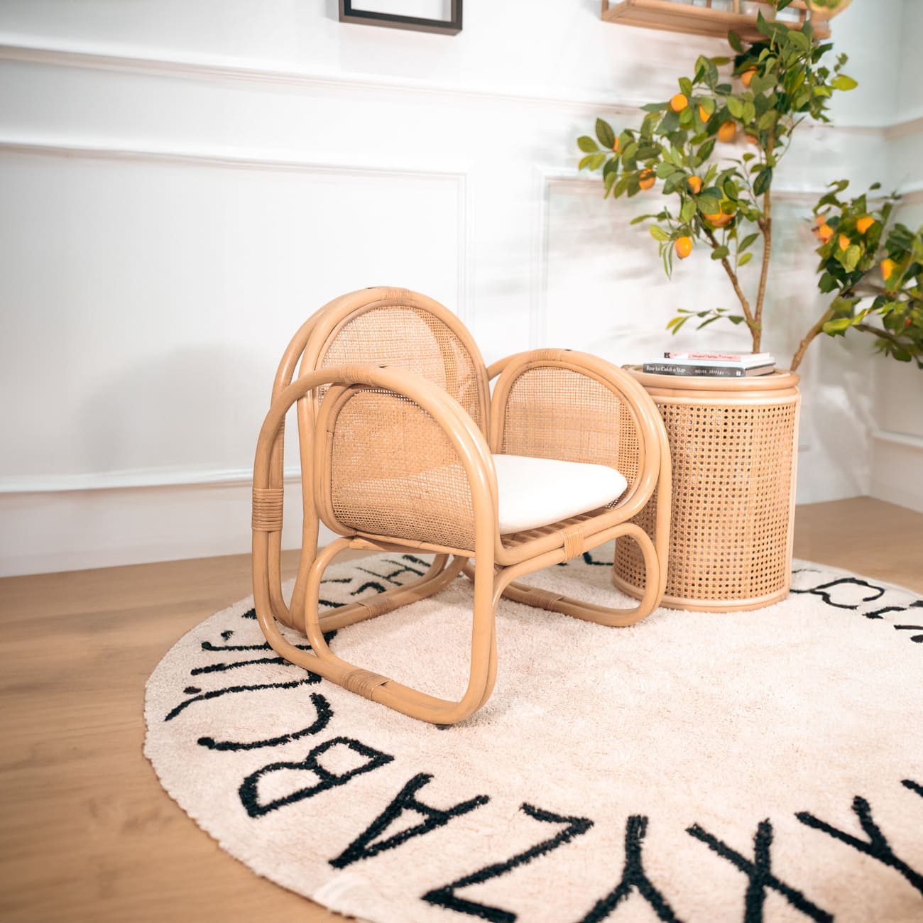 Side view of child-sized rattan Willow Lounge Chair by MOMIJI with a side table on a rug.