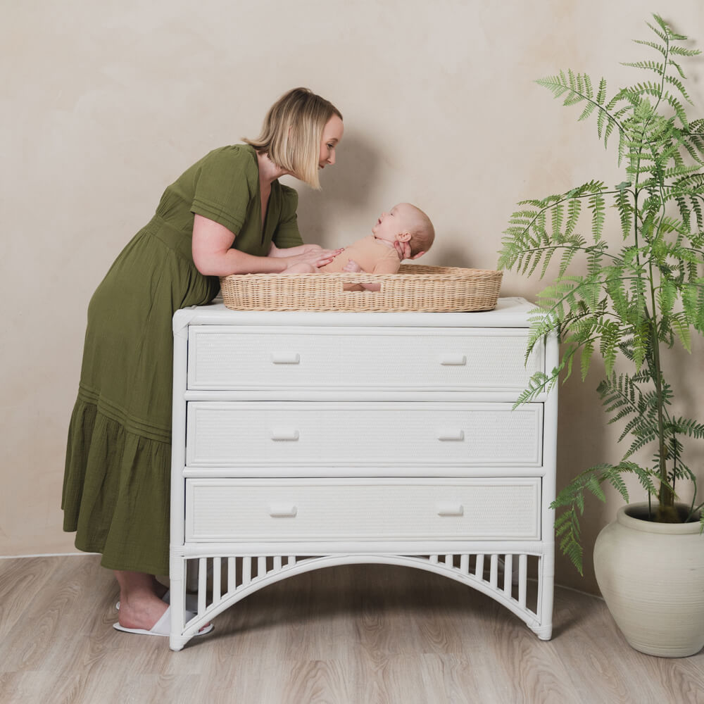 Woman changing a baby in the Xander Changing Basket by MOMIJI on a white dresser with a plant in the background.