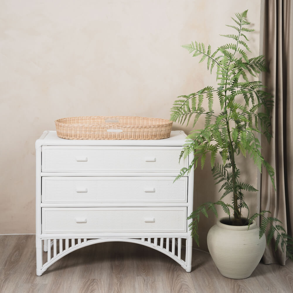 Xander Changing Basket by MOMIJI placed on a white dresser with a potted plant beside it.