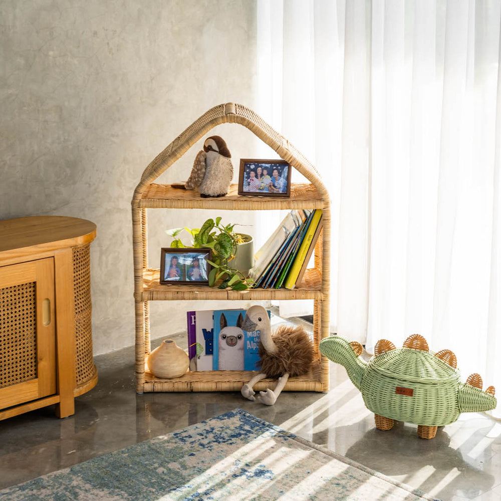 Handcrafted Alaya house shelf by MOMIJI made from rattan wicker in beige natural color, styled with toys and framed photos in a room with a wooden cabinet and a mint green dinosaur rattan basket.