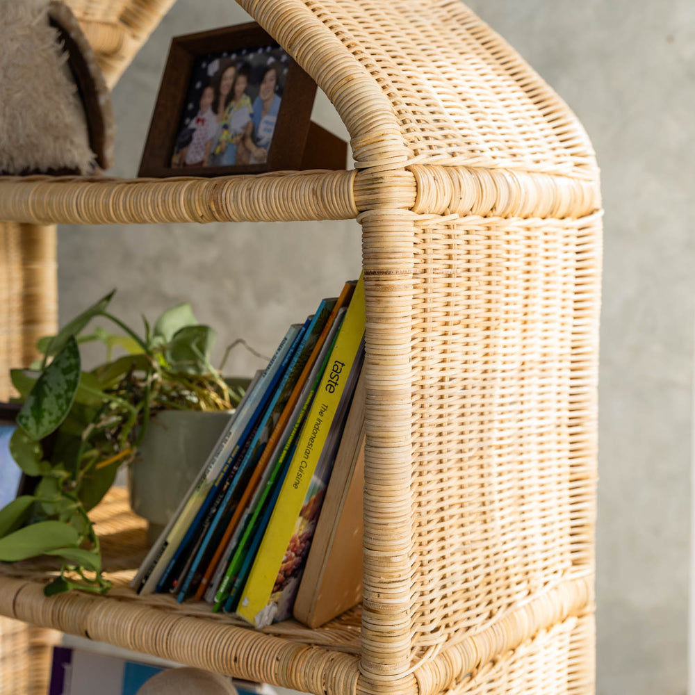 Side view of the handcrafted rattan wicker Alaya house shelf by MOMIJI with books and a photo frame, highlighting the neat and sturdy woven rattan texture against a neutral background.