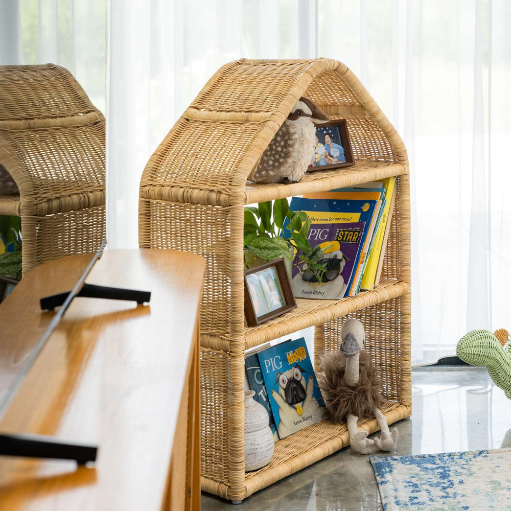 Angled view of the handcrafted rattan wicker Alaya house shelf by MOMIJI, styled with children’s books and toys, showing the fully woven structure in a room setting.