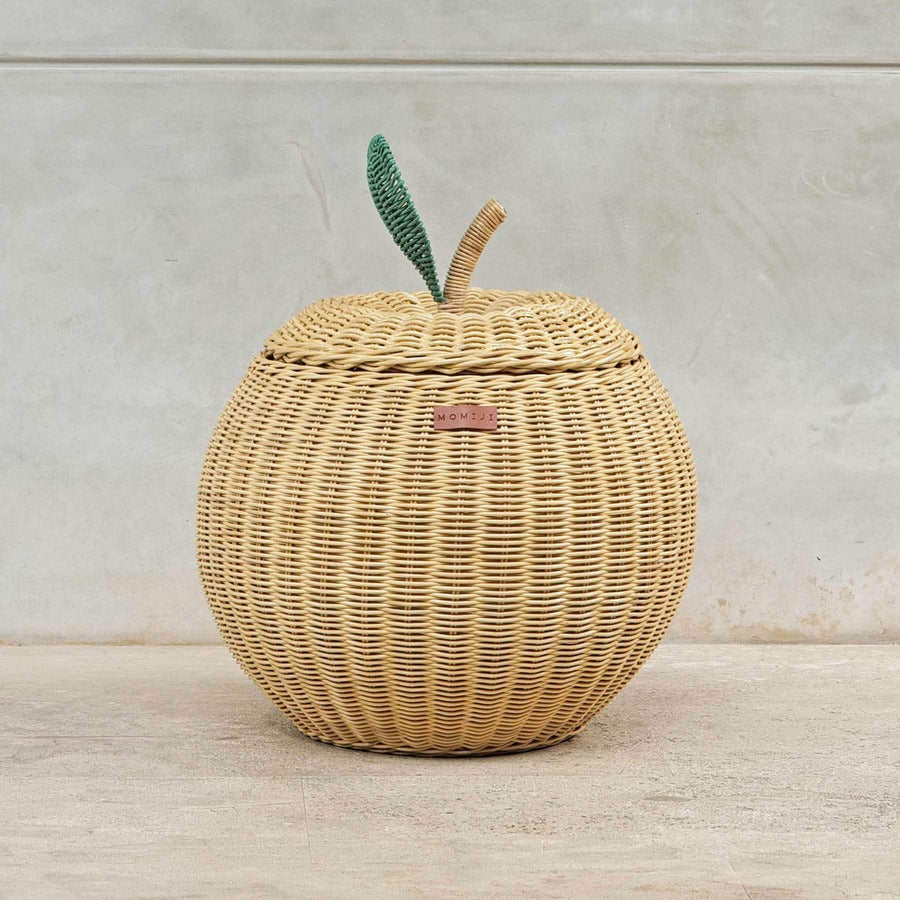 Front view of a handcrafted natural beige rattan wicker apple storage basket in medium size by MOMIJI, showing the woven design, MOMIJI label, and lid with green leaf and natural stem on the lid.