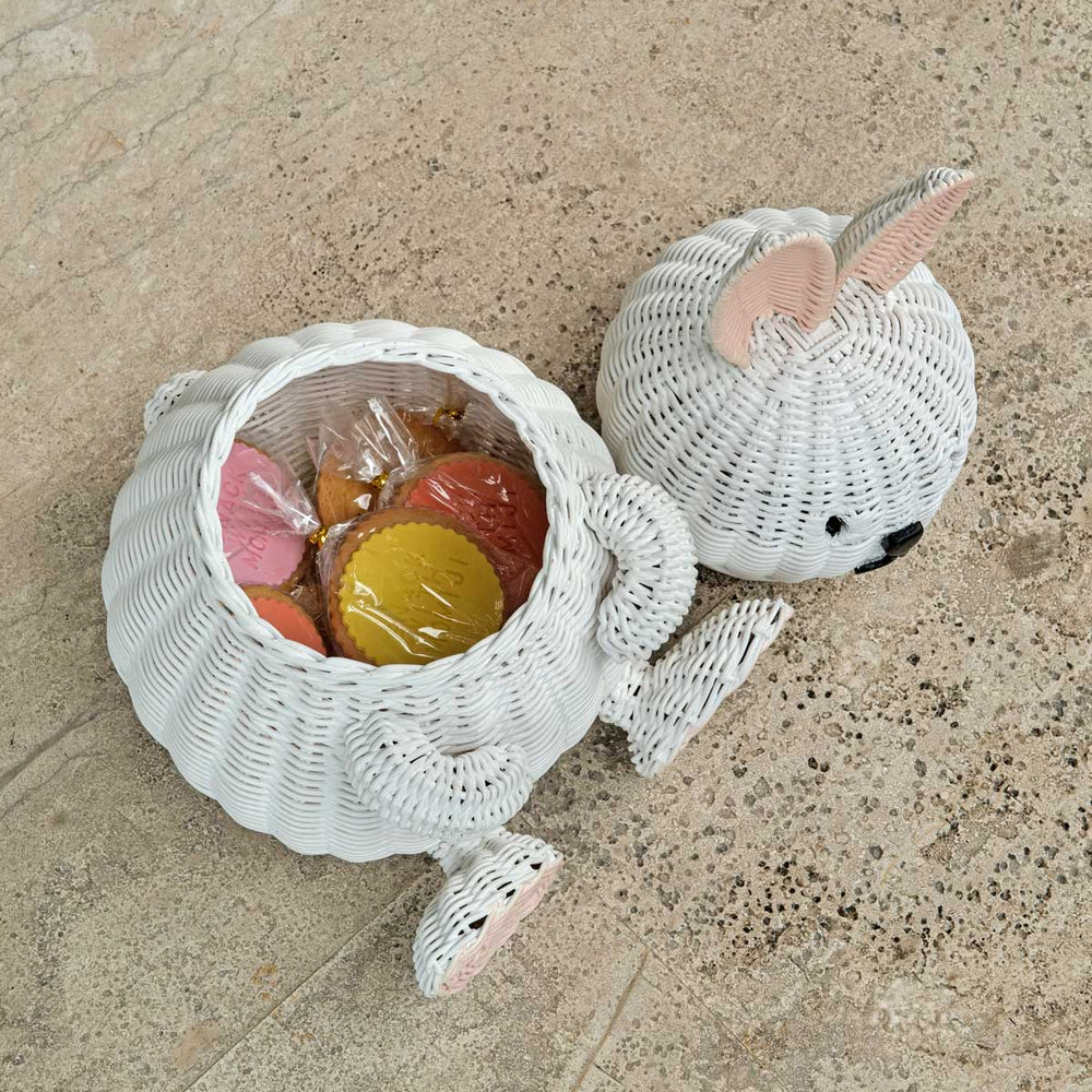 Top view of a handcrafted white rattan wicker bunny basket by MOMIJI with the lid off, filled with cookies on a textured surface.