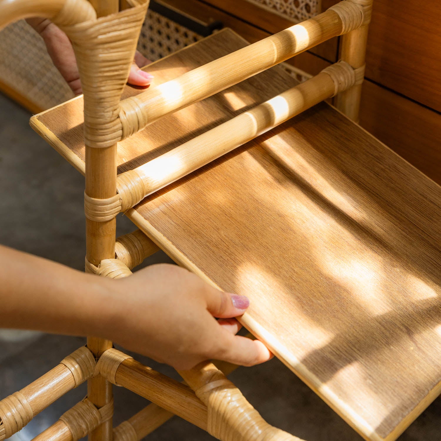 Person holding the adjustable step wooden board of a handcrafted rattan Leon Montessori learning tower by MOMIJI.