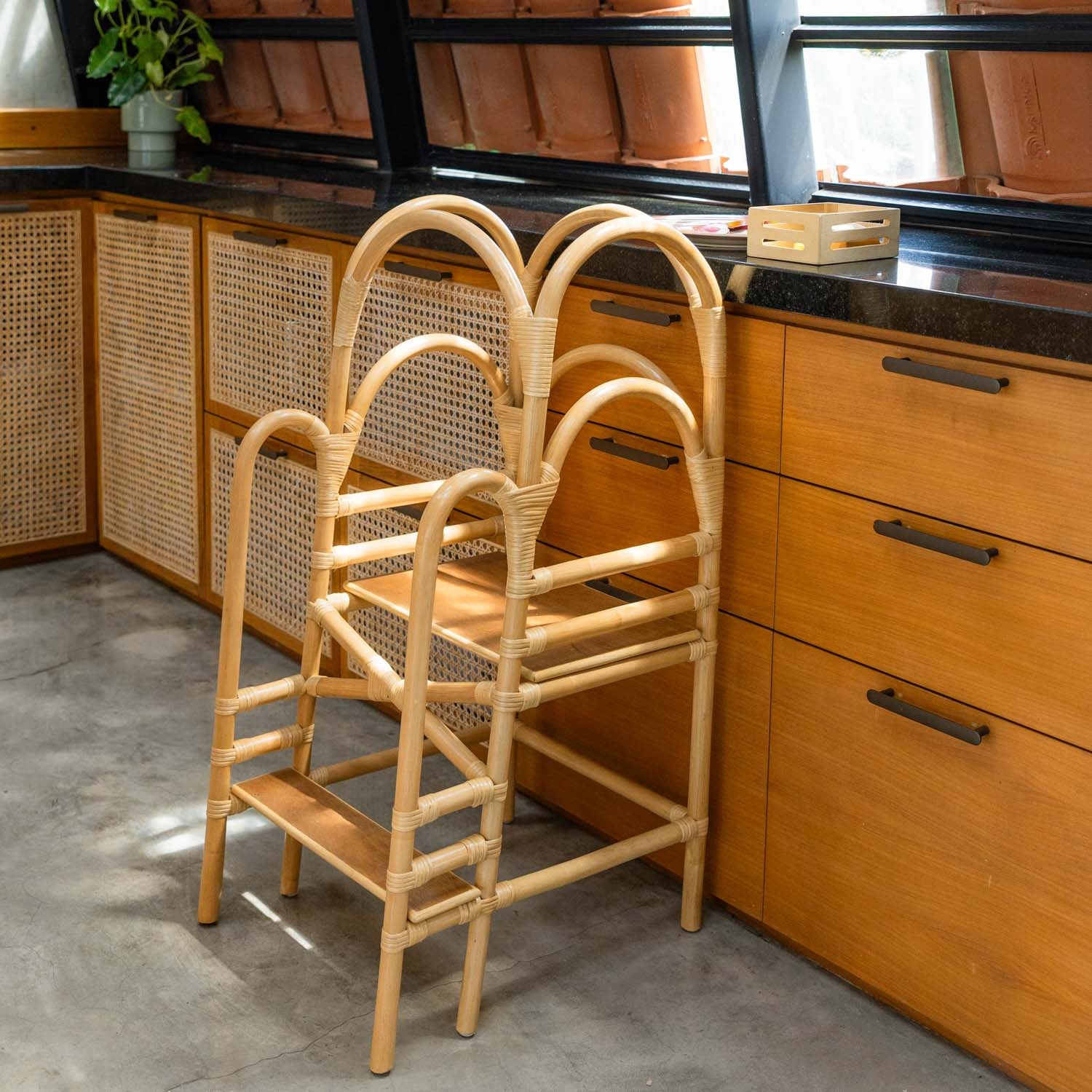 Handcrafted rattan wicker Leon Montessori learning tower by MOMIJI in a kitchen, highlighting the reinforced frame and safety support design.