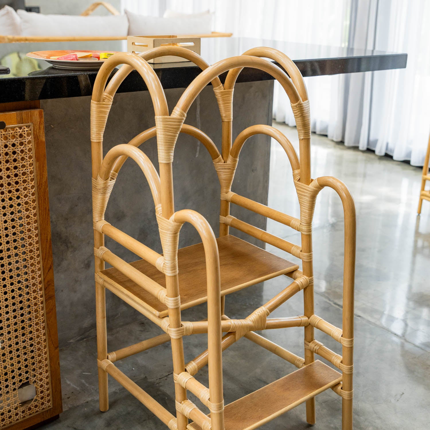 Handcrafted rattan wicker Leon Montessori learning tower by MOMIJI with an adjustable step shelf, styled in a kitchen space.