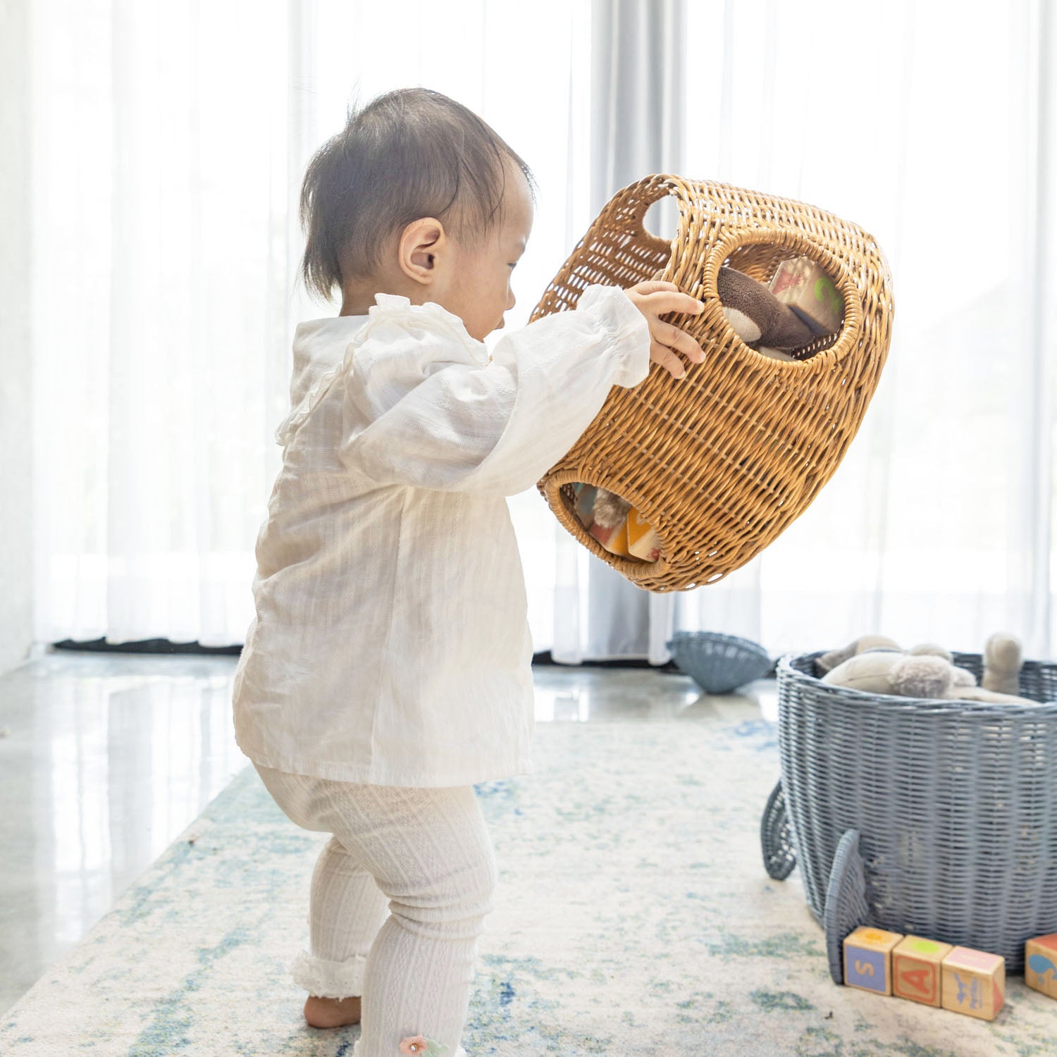Child holding the middle tier of the handcrafted rattan wicker spaceship storage and basket by MOMIJI filled with toys, separated from the lid and bottom tier in a room setting.