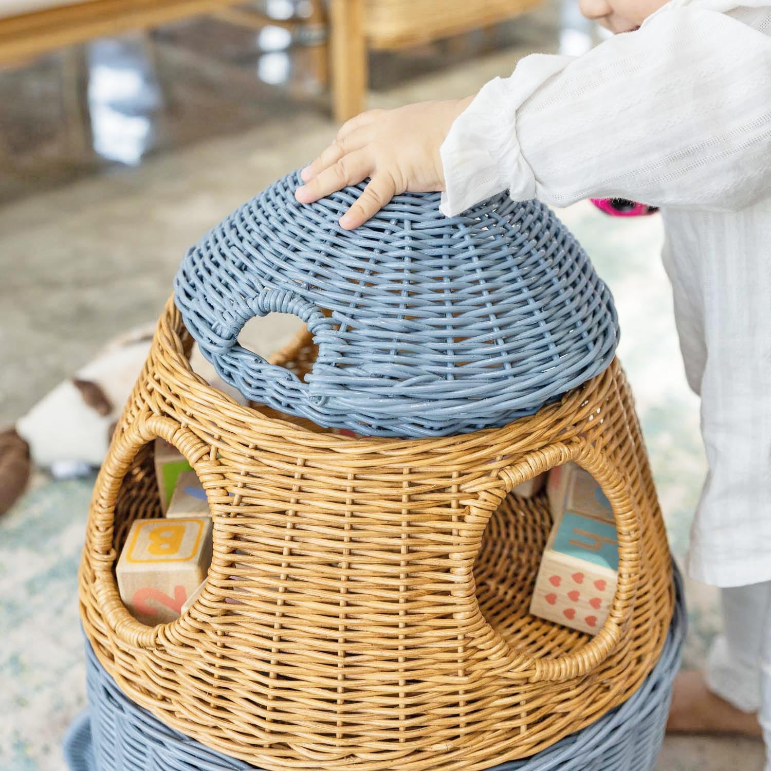 Close-up of the top and middle tiers of the handcrafted rattan wicker spaceship storage basket by MOMIJI, in grey lid and brown tier with round window details, colorful blocks inside, and neat woven texture.