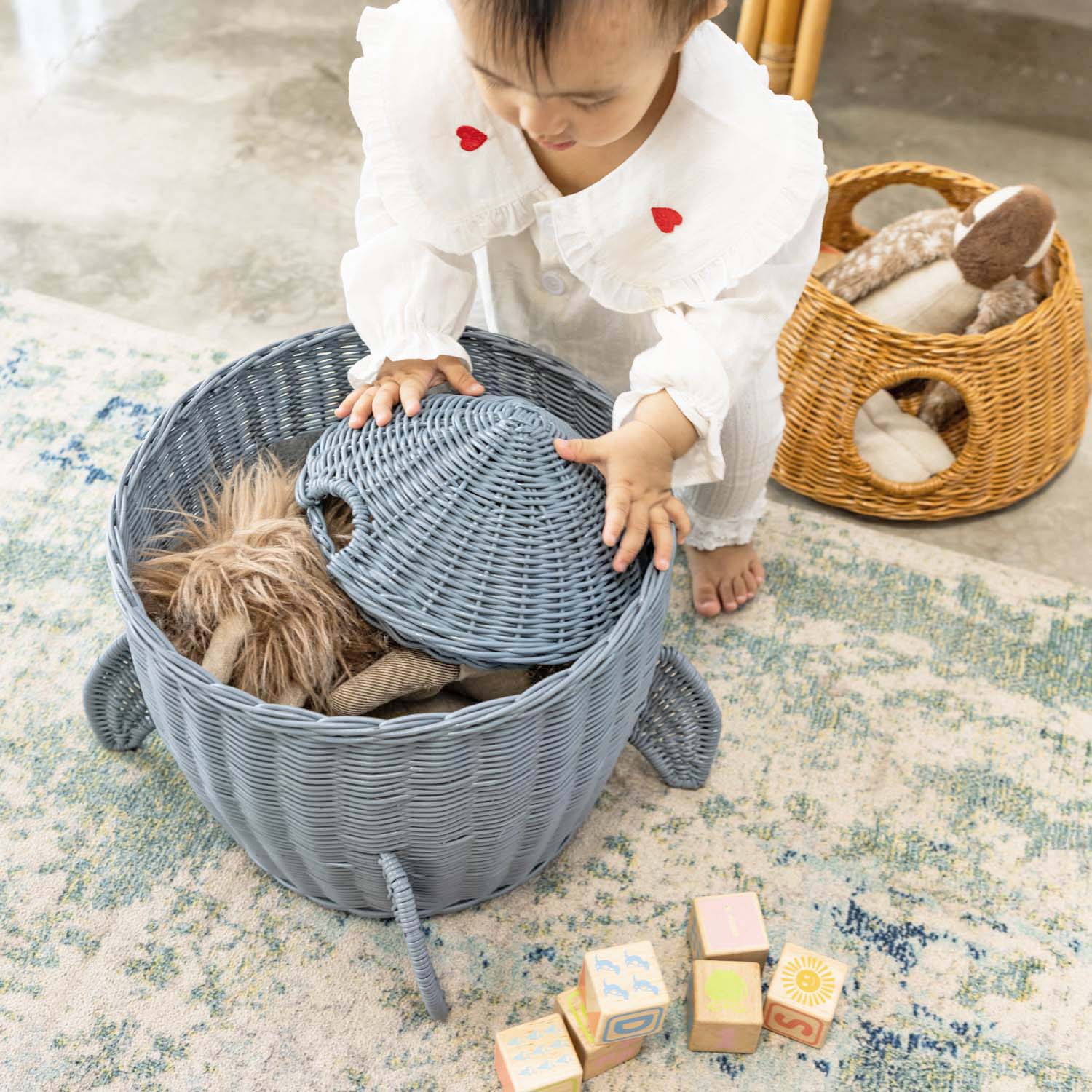 Child placing the lid onto the bottom tier of the handcrafted rattan wicker spaceship storage and basket by MOMIJI, with the middle tier positioned behind it in a room setting.
