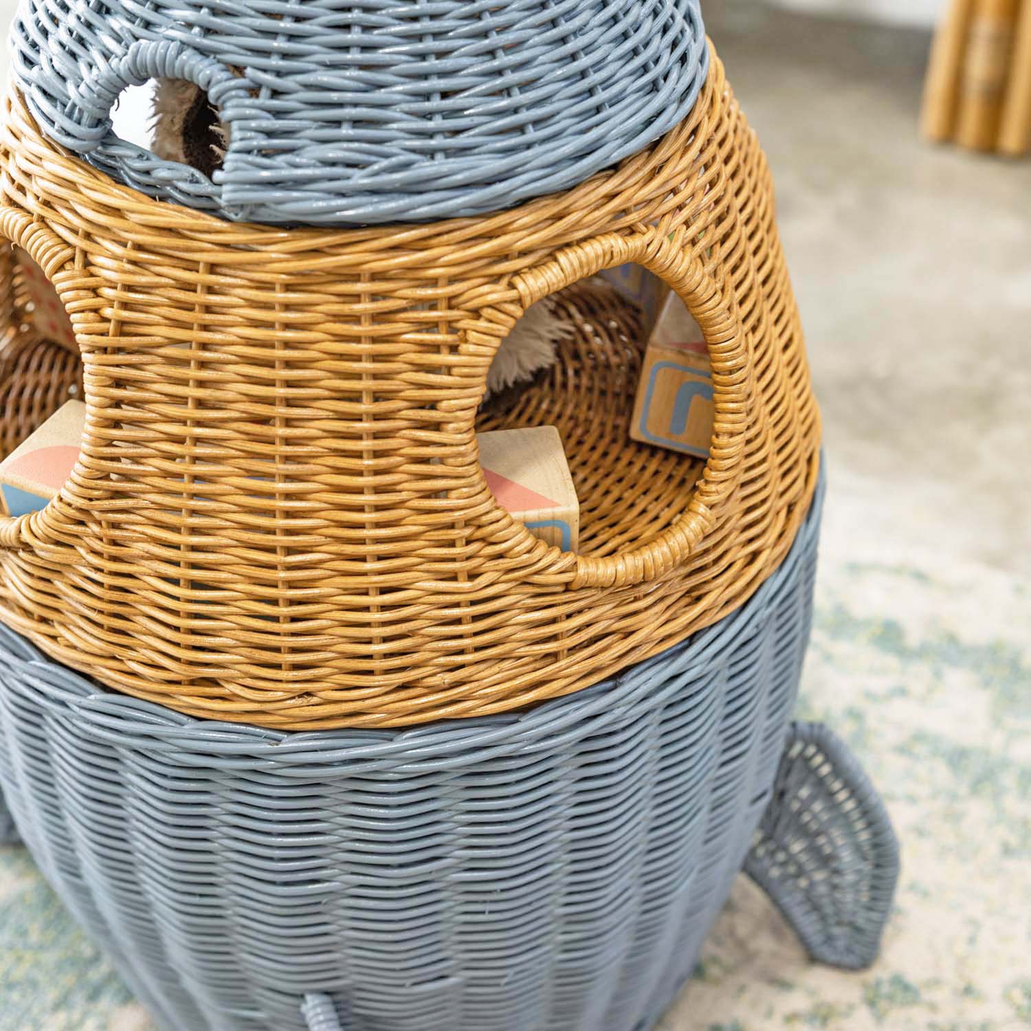 Detail view of round window of the handcrafted rattan wicker spaceship storage and basket by MOMIJI, showing woven texture on a carpeted floor.