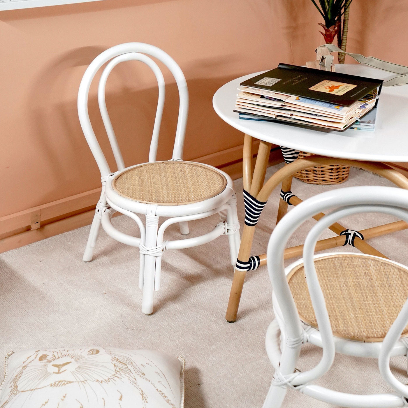 Two Aulia Kids Chairs by MOMIJI without cushions, featuring white rattan frames and natural handwoven rattan seats, placed on a rug beside an Aulia Kids Table with books in an indoor setting.
