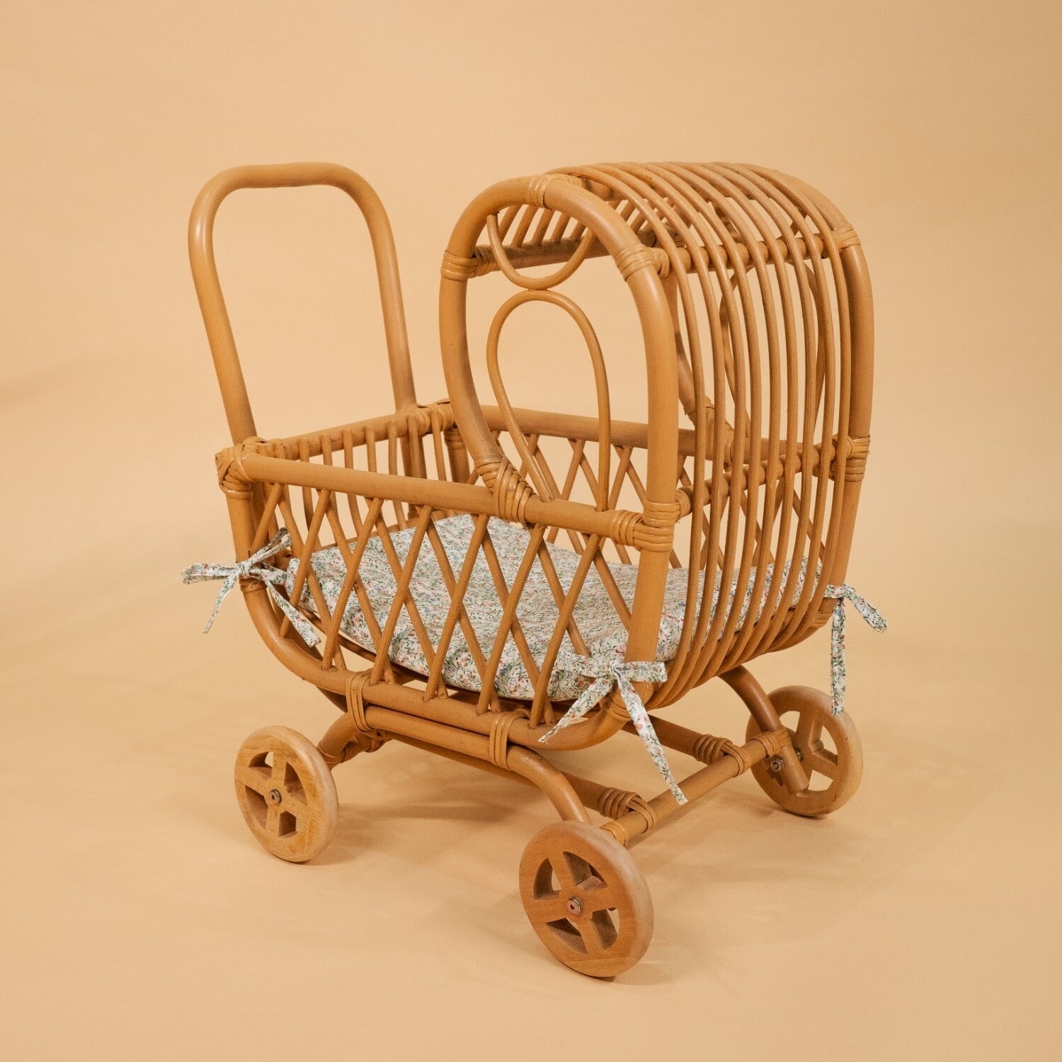 Side view of the handwoven rattan Layla Toy Stroller by MOMIJI in natural with a seat pad inside.